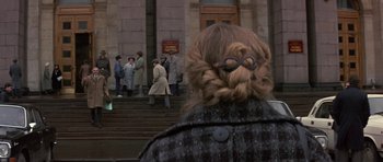 Movie still from “The Russia House” (1990), directed by Fred Schepisi – A woman with a bun and glasses is looking at a group of people on the steps; Medium shot, High angle