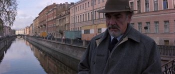 Movie still from “The Russia House” (1990), directed by Fred Schepisi – An older man wearing a hat standing next to a river; Medium shot, Low angle