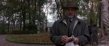 Movie still from “The Russia House” (1990), directed by Fred Schepisi – An older man in a hat and a coat is holding a book; Medium shot, Over the shoulder angle