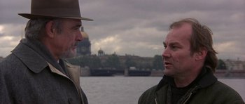 Movie still from “The Russia House” (1990), directed by Fred Schepisi – Two men standing next to each other near a body of water; Close Up shot, Over the shoulder angle