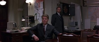 Movie still from “The Russia House” (1990), directed by Fred Schepisi – Two men in suits sitting at a table in a room; Medium shot, Over the shoulder angle