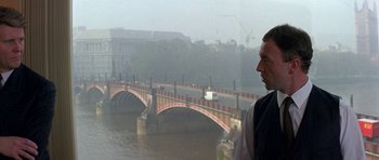 Movie still from “The Russia House” (1990), directed by Fred Schepisi – A man standing next to a river with a bridge in the background; Medium shot, Over the shoulder angle