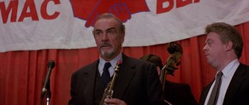 Movie still from “The Russia House” (1990), directed by Fred Schepisi – A man in a suit and tie holding a saxophone in front of an audience; Close Up shot, Low angle