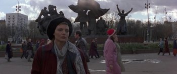 Movie still from “The Russia House” (1990), directed by Fred Schepisi – A group of people walking on a sidewalk near a statue; Medium shot, Over the shoulder angle
