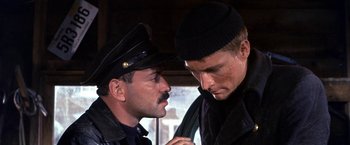 Movie still from “The Russians Are Coming the Russians Are Coming” (1966), directed by Norman Jewison – Two men in black jackets and a black hat are talking; Close Up shot, Over the shoulder angle
