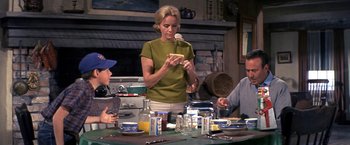 Movie still from “The Russians Are Coming the Russians Are Coming” (1966), directed by Norman Jewison – A woman standing at a dining table with two men and a child; Medium shot, Over the shoulder angle