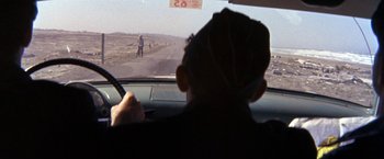 Movie still from “The Russians Are Coming the Russians Are Coming” (1966), directed by Norman Jewison – A man driving a car on the side of a road; Wide shot, Over the shoulder angle