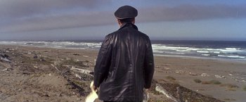 Movie still from “The Russians Are Coming the Russians Are Coming” (1966), directed by Norman Jewison – A man in a leather jacket and hat looking out at the ocean; Wide shot, High angle
