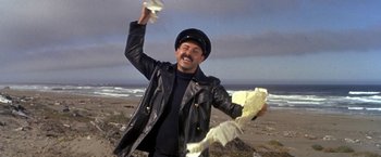 Movie still from “The Russians Are Coming the Russians Are Coming” (1966), directed by Norman Jewison – A man in a black leather jacket throwing papers in the air on the beach; Medium shot, Low angle