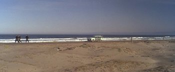 Movie still from “The Russians Are Coming the Russians Are Coming” (1966), directed by Norman Jewison – A car parked on the beach near the ocean; Extreme Wide shot, High angle