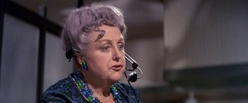 Movie still from “The Russians Are Coming the Russians Are Coming” (1966), directed by Norman Jewison – An older woman with purple hair is wearing a microphone; Close Up shot, Over the shoulder angle