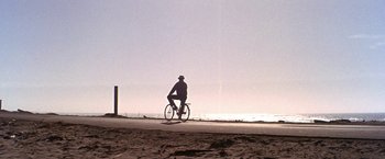 Movie still from “The Russians Are Coming the Russians Are Coming” (1966), directed by Norman Jewison – A man riding a bike down a road next to the ocean; Extreme Wide shot, Low angle