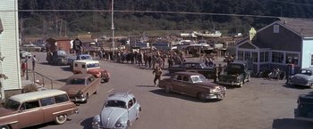 Movie still from “The Russians Are Coming the Russians Are Coming” (1966), directed by Norman Jewison – A group of people standing next to cars on a street; Extreme Wide shot, High angle