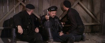 Movie still from “The Russians Are Coming the Russians Are Coming” (1966), directed by Norman Jewison – A group of men sitting on the ground holding guns; Medium shot, High angle