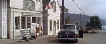 Movie still from “The Russians Are Coming the Russians Are Coming” (1966), directed by Norman Jewison – An old car parked in front of a building with an american flag on it; Extreme Wide shot, High angle