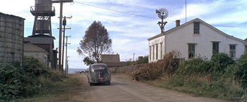 Movie still from “The Russians Are Coming the Russians Are Coming” (1966), directed by Norman Jewison – An old car driving down a dirt road near a windmill; Extreme Wide shot, High angle