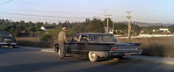 Movie still from “The Russians Are Coming the Russians Are Coming” (1966), directed by Norman Jewison – An older man standing next to an old car; Wide shot, Over the shoulder angle