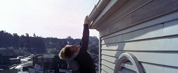 Movie still from “The Russians Are Coming the Russians Are Coming” (1966), directed by Norman Jewison – A woman reaching up to reach the roof of a house; Wide shot, Low angle