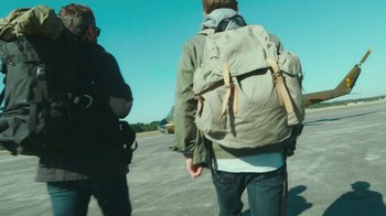 Movie still from “The Sacrament” (2013), directed by Ti West – Two people with backpacks walking on a runway; Medium shot, Low angle
