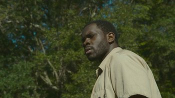 Movie still from “The Sacrament” (2013), directed by Ti West – A man in a tan shirt is standing in front of a tree; Close Up shot, Low angle