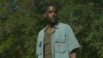 Movie still from “The Sacrament” (2013), directed by Ti West – A man standing in front of a tree looking to his left; Medium shot, Low angle