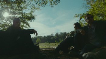 Movie still from “The Sacrament” (2013), directed by Ti West – Two people sitting on the ground near a forest; Wide shot, Low angle