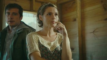 Movie still from “The Sacrament” (2013), directed by Ti West – A woman with a headband is sitting in front of a wooden wall; Close Up shot, Over the shoulder angle