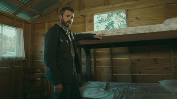 Movie still from “The Sacrament” (2013), directed by Ti West – A man standing in front of a bed in a room; Medium shot, Low angle