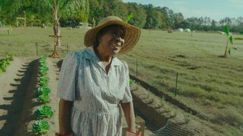 Movie still from “The Sacrament” (2013), directed by Ti West – An older woman wearing a straw hat standing in a field; Medium shot, High angle