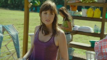Movie still from “The Sacrament” (2013), directed by Ti West – A woman in a purple tank top standing next to a bench; Medium shot, Over the shoulder angle