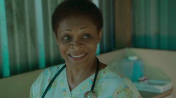 Movie still from “The Sacrament” (2013), directed by Ti West – An older woman with a stethoscope around her neck; Close Up shot, Over the shoulder angle