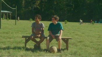 Movie still from “The Sacrament” (2013), directed by Ti West – Two young men sitting on a bench in the grass; Wide shot, Over the shoulder angle