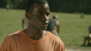 Movie still from “The Sacrament” (2013), directed by Ti West – A man in an orange t - shirt is standing in the grass; Close Up shot, Over the shoulder angle