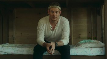 Movie still from “The Sacrament” (2013), directed by Ti West – A man sitting on top of a bed wearing a headband; Close Up shot, Low angle