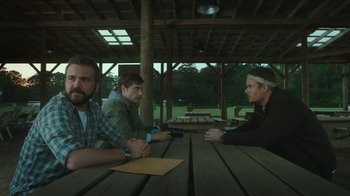 Movie still from “The Sacrament” (2013), directed by Ti West – A group of men sitting at a picnic table; Medium shot, Over the shoulder angle