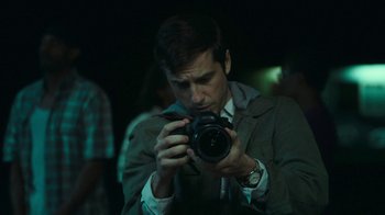 Movie still from “The Sacrament” (2013), directed by Ti West – A man taking a picture with a camera; Close Up shot, Over the shoulder angle