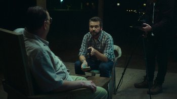 Movie still from “The Sacrament” (2013), directed by Ti West – A man sitting on a chair in front of another man; Medium shot, Over the shoulder angle