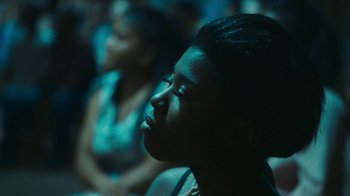 Movie still from “The Sacrament” (2013), directed by Ti West – A woman sitting in a crowd of people at a concert; Close Up shot, Over the shoulder angle