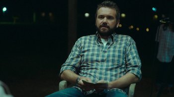 Movie still from “The Sacrament” (2013), directed by Ti West – A man sitting in a chair holding a game controller; Medium shot, Over the shoulder angle