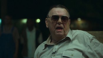 Movie still from “The Sacrament” (2013), directed by Ti West – An older man wearing sunglasses and a tan shirt; Close Up shot, Over the shoulder angle
