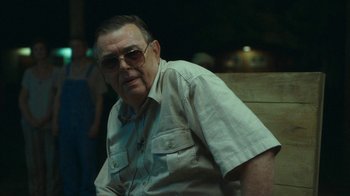Movie still from “The Sacrament” (2013), directed by Ti West – An older man wearing sunglasses sitting on top of a bench; Medium shot, Over the shoulder angle