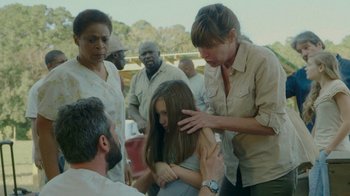Movie still from “The Sacrament” (2013), directed by Ti West – A group of people standing around a woman; Medium shot, High angle