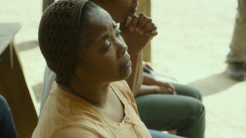 Movie still from “The Sacrament” (2013), directed by Ti West – A woman sitting next to another woman with her hands clasped together; Close Up shot, Over the shoulder angle