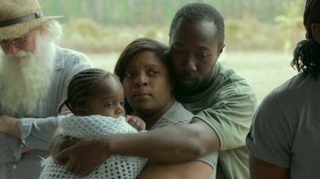 Movie still from “The Sacrament” (2013), directed by Ti West – A man and a woman holding a child in their arms; Medium shot, High angle
