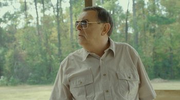 Movie still from “The Sacrament” (2013), directed by Ti West – An older man wearing glasses and a tan shirt; Close Up shot, Over the shoulder angle