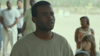 Movie still from “The Sacrament” (2013), directed by Ti West – A young man is standing in front of a group of people; Close Up shot, Over the shoulder angle
