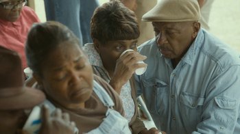 Movie still from “The Sacrament” (2013), directed by Ti West – A group of people gathered around drinking from cups; Medium shot, High angle