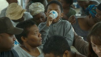 Movie still from “The Sacrament” (2013), directed by Ti West – A boy is drinking from a cup while a woman looks on; Close Up shot, High angle