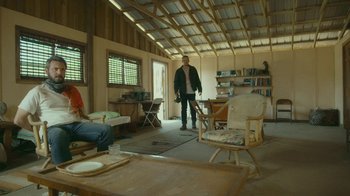 Movie still from “The Sacrament” (2013), directed by Ti West – A man is standing in a living room with two other people; Wide shot, High angle