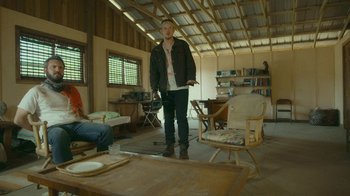 Movie still from “The Sacrament” (2013), directed by Ti West – A man standing in a living room holding a remote control; Wide shot, Low angle